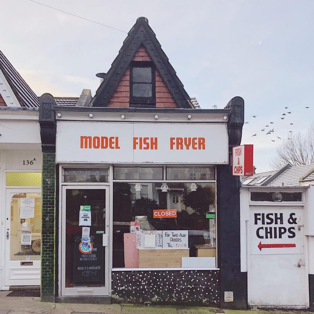 small shopfront facade with a pitched roof and an orange sign
