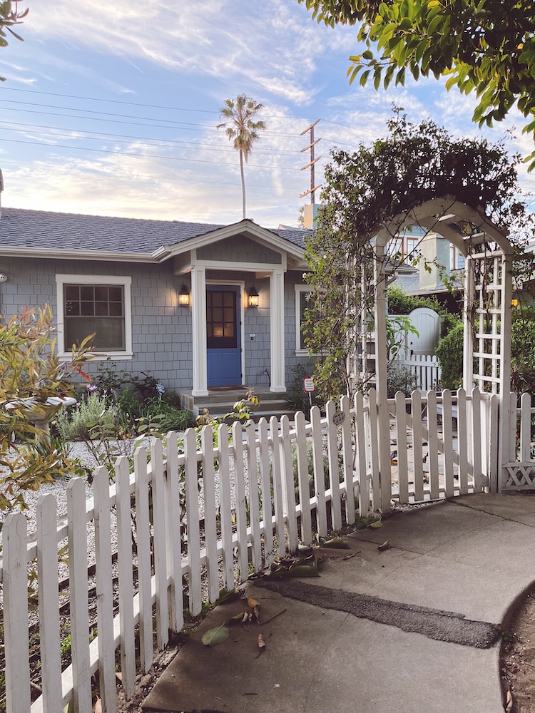 a blue single-story house surrounded by a white picket fence in Venice, LA