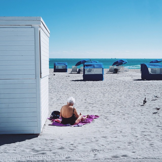 A lady lying on a pink beach towel next to a white wooden beach hut in Miami