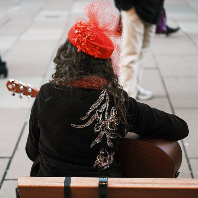 Picture of a lady in a red hat sitting on a bench playing a guitar in Bath, Somerset