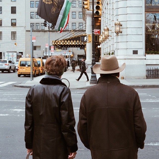 A couple crossing a street in New York, one wearing a cowboy hat