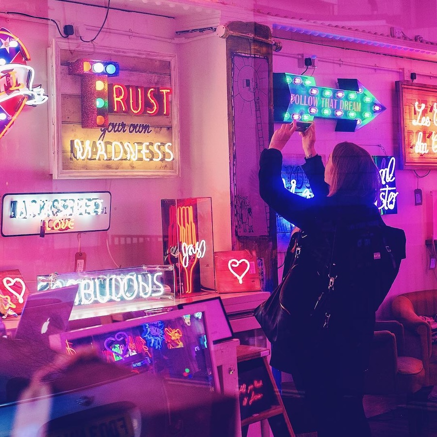 Picture of a girl in a room full of neon signs taking a photograph