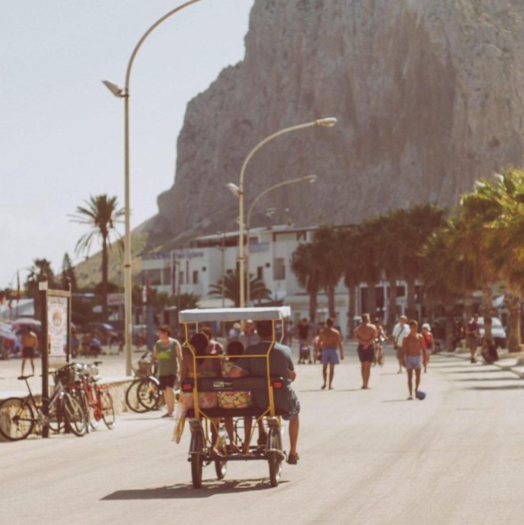 a picture of a group of people cycling in a covered bike along a street towards a mountain