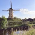 Traditional Dutch windmill on a grassy mound beside a canal at golden hour, near Fort NOXX, Hoofddorp, North Holland