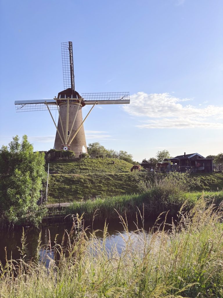 Traditional Dutch windmill on a grassy mound beside a canal at golden hour, near Fort NOXX, Hoofddorp, North Holland