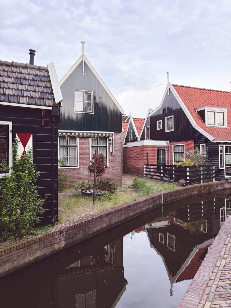 Traditional black and red timber-framed Dutch houses reflected in a narrow canal, Volendam, North Holland