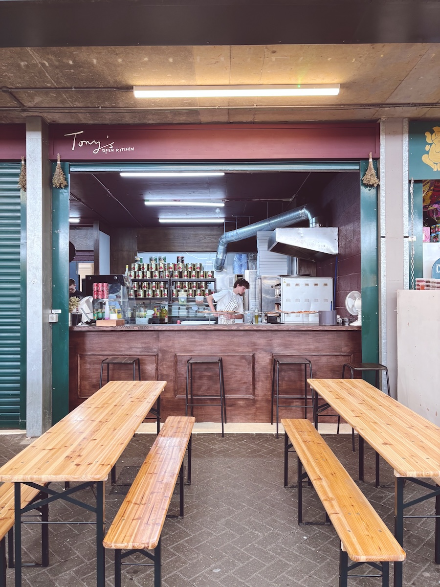 Tony’s Open Kitchen at Brighton Open Market, with wooden communal tables and the open kitchen behind