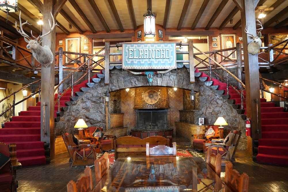 Historic lobby at El Rancho in Gallup, New Mexico, with twin staircases, timber beams and stone fireplace