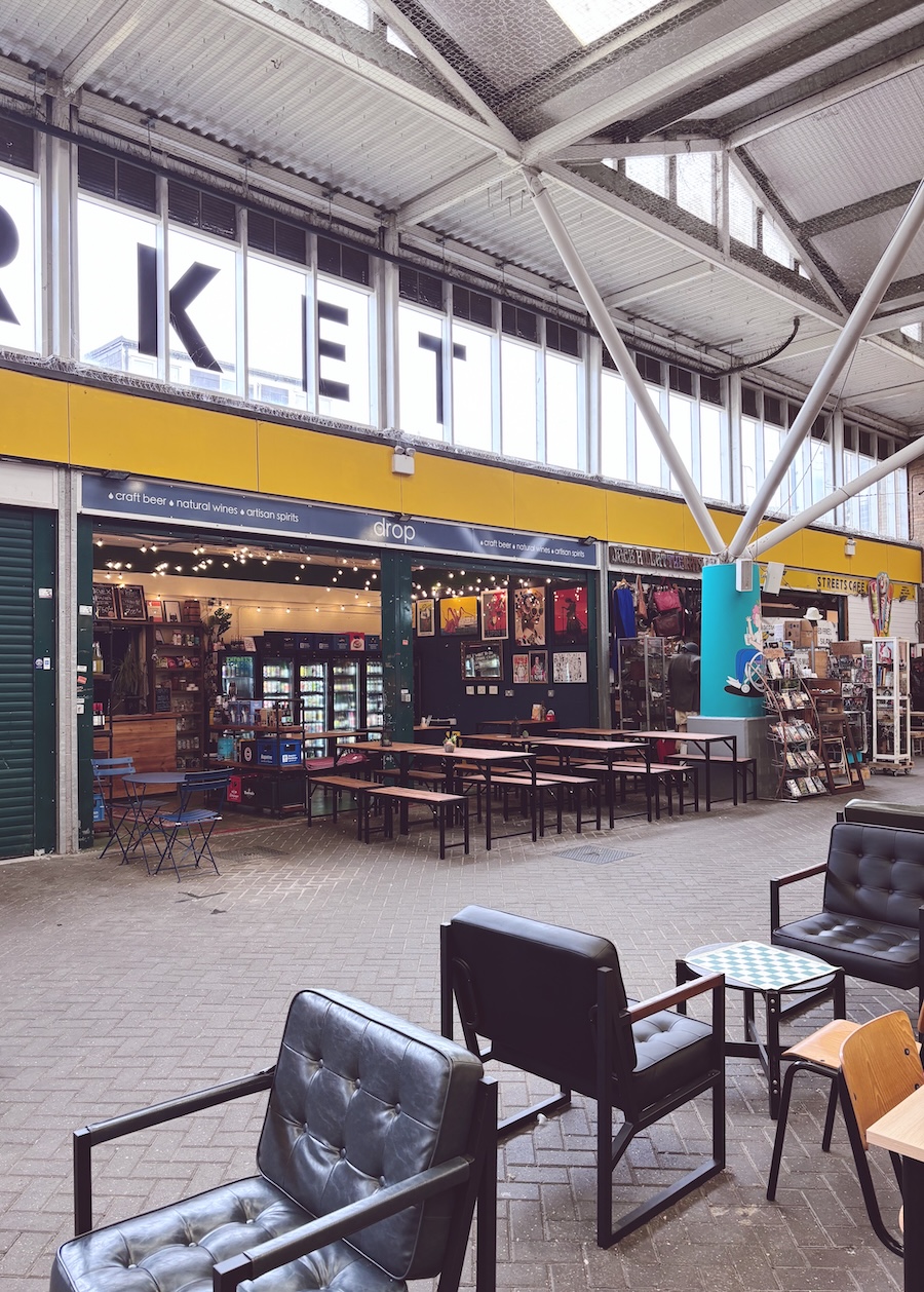 Seating area inside Brighton Open Market, with The Drop bar and market stalls in the background