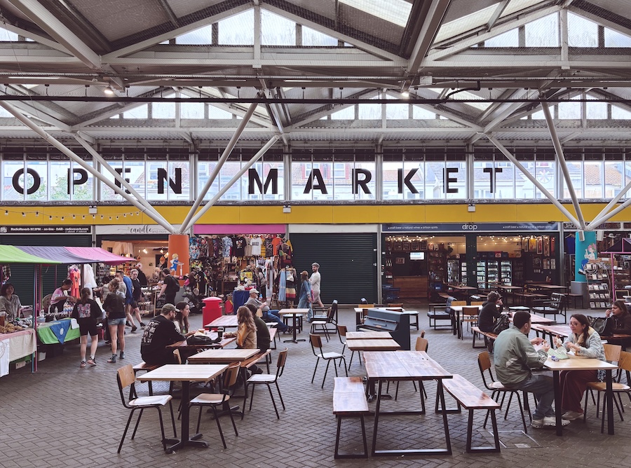 Main hall of Brighton Open Market with communal tables, independent stalls and people eating and shopping