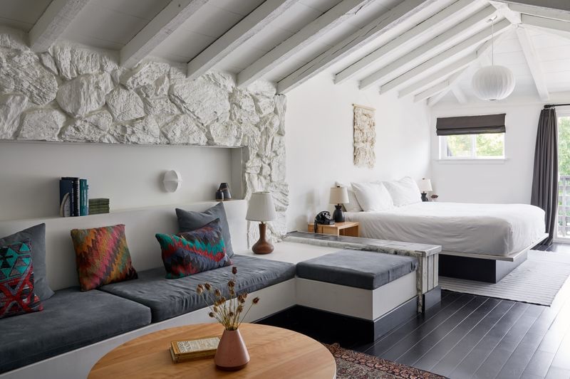 Guest room at Scribner’s Catskill Lodge with white stone wall, vaulted ceiling and colourful cushions