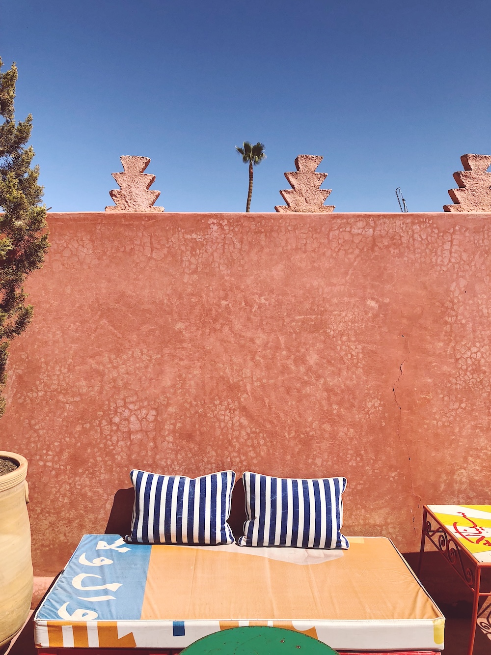 Pop-art daybed with blue striped cushions against a terracotta wall on a rooftop terrace in Marrakech